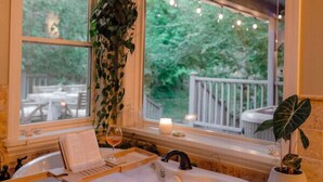 A bathroom with a large bathtub, a window with a view of a deck, and a potted plant on the windowsill. - Luxury Home, Hot Tub Walk To Downtown Nevada City (Nevada City)