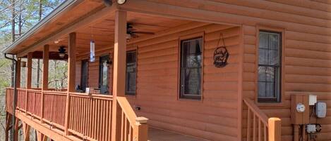 A wooden cabin with a covered porch, a front door, and a small front yard.