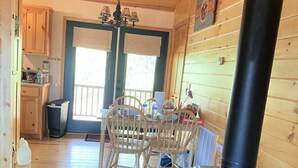 L’intérieur d’une cabane est doté d’un plancher en bois, d’une table à manger avec des chaises, d’un poêle à bois noir et d’un coin cuisine avec des armoires en bois et un réfrigérateur.