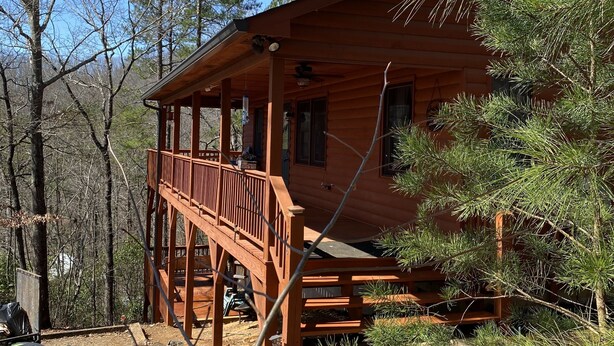 Une cabane en bois dotée d’un porche couvert et d’une terrasse, entourée d’arbres.