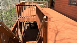 Une terrasse en bois avec un escalier menant à une zone abritée, le tout entouré d’arbres.