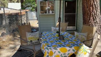 An outdoor patio with a table covered by a tablecloth with a lemon pattern, surrounded by chairs with matching cushions.