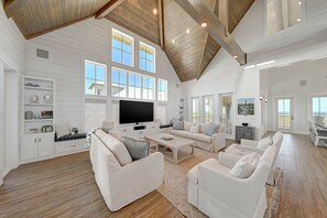 Relax in this spacious living area with a high ceiling and large windows offering a coastal view.