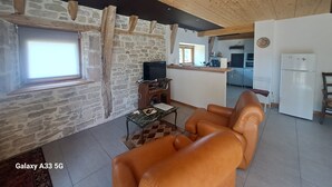 A spacious living area with a stone wall, wooden ceiling, and a modern kitchen in the background. - Quercy farmhouse in the heart of the Lot, ideal for family with outdoor space  (Le Bourg)