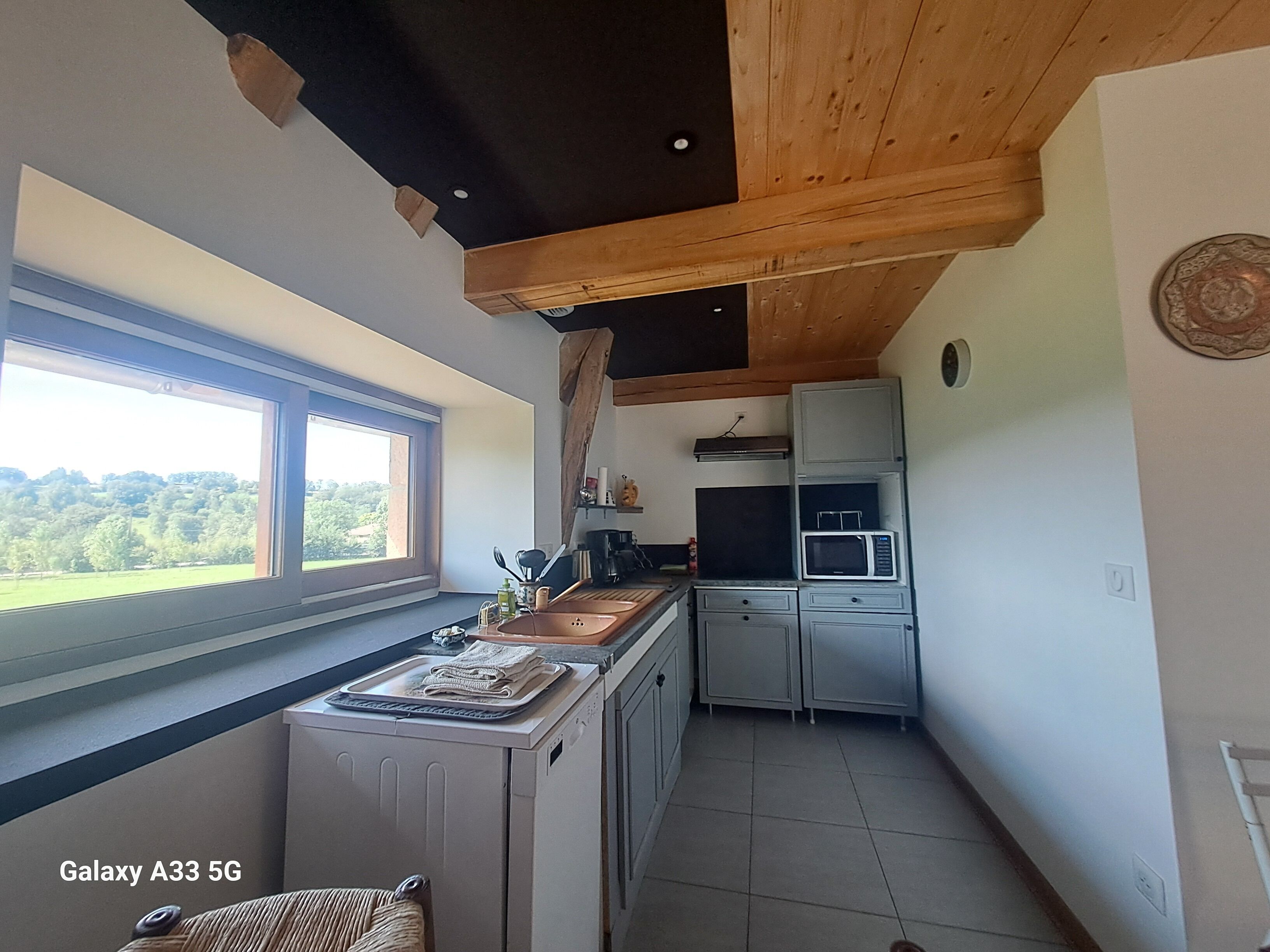 A compact kitchen with a window, wooden ceiling beams, and a microwave.