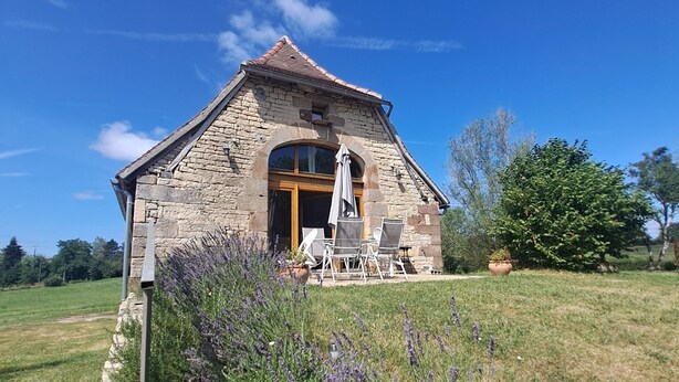 A stone building with a tiled roof, a large arched window, and a patio with outdoor furniture. - Quercy farmhouse in the heart of the Lot, ideal for family with outdoor space  (Le Bourg)