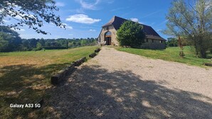 A stone building with a gravel driveway leading to a wooden door, surrounded by grassy fields and trees. - Quercy farmhouse in the heart of the Lot, ideal for family with outdoor space  (Le Bourg)