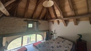 A bedroom with a wooden ceiling, a bed with a floral bedspread, a window with a view of the outdoors, and a small table with a lamp. - Quercy farmhouse in the heart of the Lot, ideal for family with outdoor space  (Le Bourg)