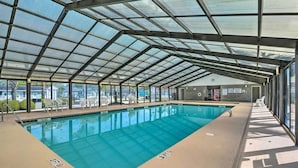 En indendørs swimmingpool med glasloft, transparente liggestole og udsigt udad.