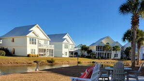 En ejendom ved stranden med hvide liggestole og et poolområde.