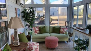 Et solrum med ventilator, store vinduer og en grøn sofa.
