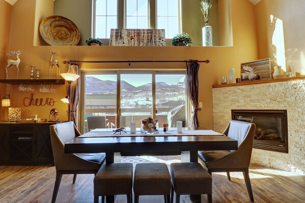 A dining area with a large table and chairs, a fireplace, and a view of mountains through large windows.