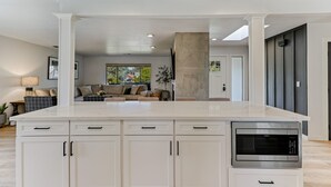 A modern kitchen with a large island, white cabinetry, and a built-in microwave. - ***Pineland Place*** (Redding)