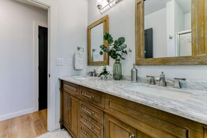 A bathroom with two sinks, wooden cabinets, a large mirror, and a vase with greenery. - ***Pineland Place*** (Redding)