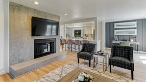 A modern living room with a fireplace, a flat-screen TV, and a dining area with bar stools. - ***Pineland Place*** (Redding)