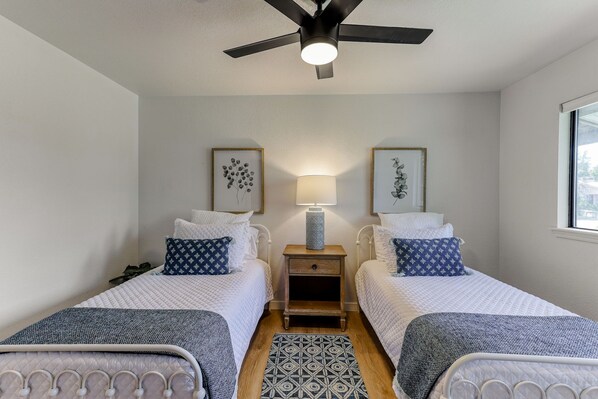 A bedroom with two beds, a ceiling fan, a nightstand with a lamp, and framed artwork on the wall. - ***Pineland Place*** (Redding)