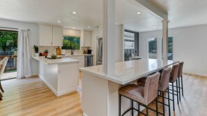 A modern kitchen with white cabinetry, a central island, and bar stools. - ***Pineland Place*** (Redding)