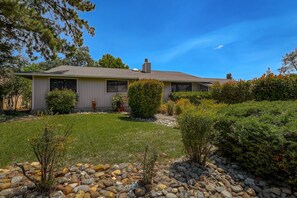 A single-story house with a sloped roof, a chimney, and a well-maintained front yard with a stone pathway leading to the entrance. - ***Pineland Place*** (Redding)