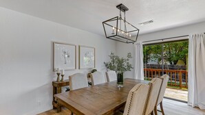 A dining area with a wooden table, four chairs, a vase with plants, and a hanging light fixture. - ***Pineland Place*** (Redding)