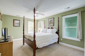 Relax in a serene bedroom with a four-poster bed, ceiling fan, and large window with blinds.