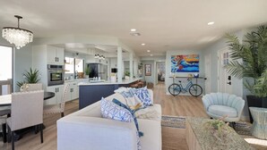 A spacious living area with a dining table, sofa, and a kitchen in the background. - Surf View Bungalow with Outstanding Ocean Views! (Encinitas)