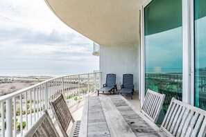 A balcony with a wooden table and two chairs, overlooking a beach and ocean.