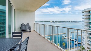 Un balcon avec une table et des chaises, donnant sur une marina où sont amarrés des bateaux, et où l’on aperçoit un pont au loin.