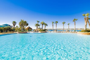 A clear blue pool with palm trees and lounge chairs, surrounded by buildings and a clear sky. - Beautiful Beach Condo; STUNNING VIEWS OF Gulf & BAY!  (Orange Beach)
