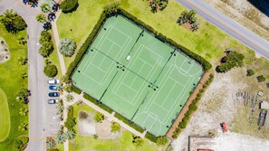 An aerial view of a tennis court surrounded by greenery and a parking lot.
