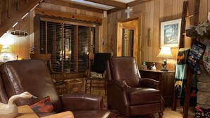 A cozy wooden interior with leather armchairs, a wooden staircase, and a rustic decor including a wooden cross and a framed picture. - Journeys End Lodging Cabins (Long Lake)