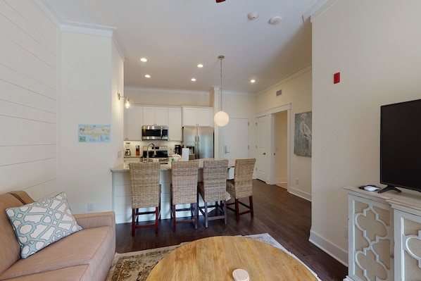 A modern living room with a sofa, a round coffee table, and a TV on a cabinet. There is a kitchen area with a dining table and chairs.