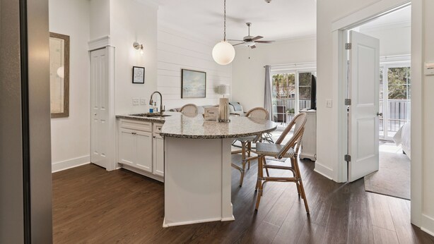 A kitchen with a central island, wooden flooring, white cabinetry, and a ceiling fan. - Village Centric Condo w/ Pool Unit 2106 First Floor (St. Simons Island)