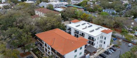 A multi-story building with a red-tiled roof, parking lot, and a view of the sea.