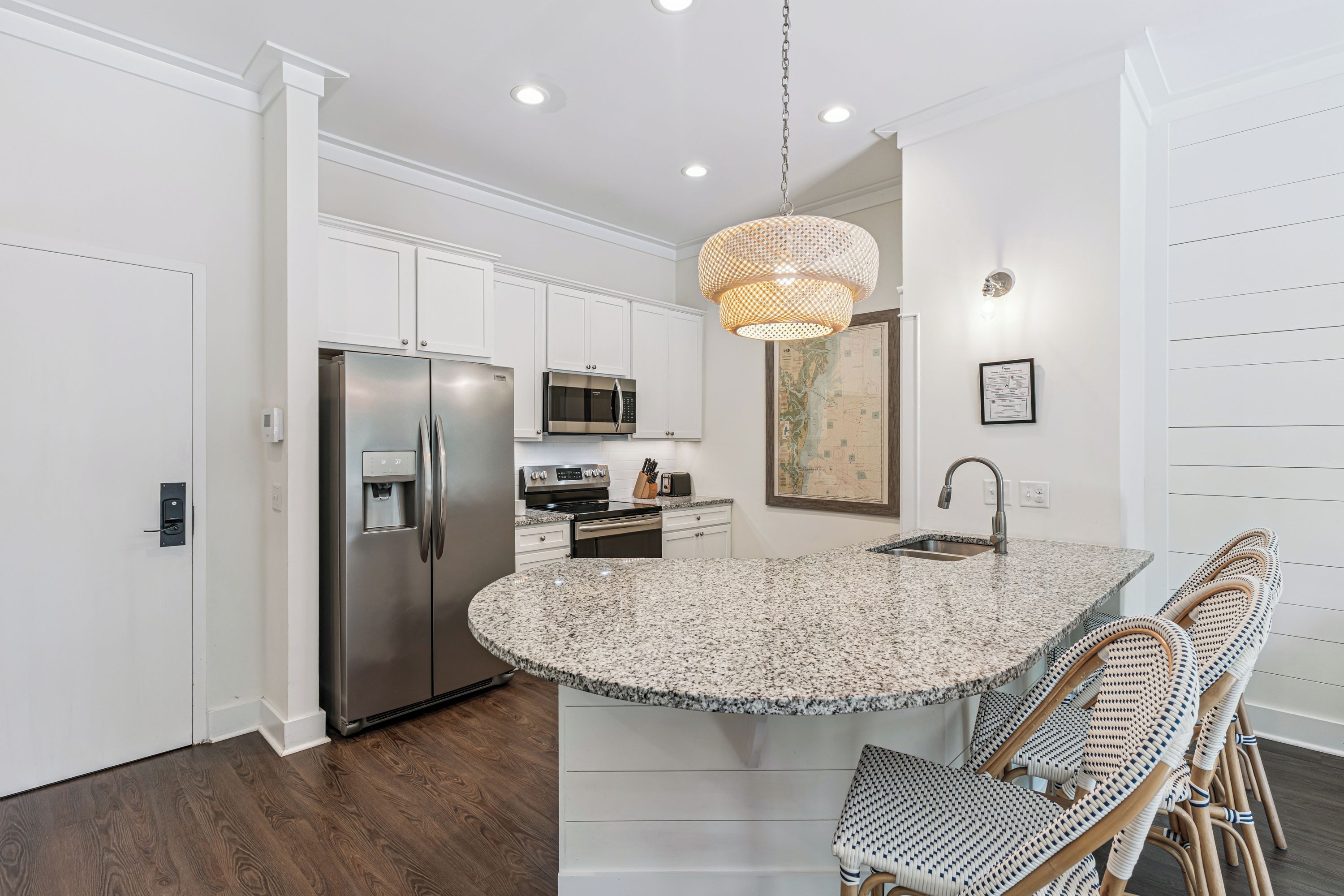 A modern kitchen with white cabinetry, stainless steel appliances, a granite countertop island, and a woven pendant light.
