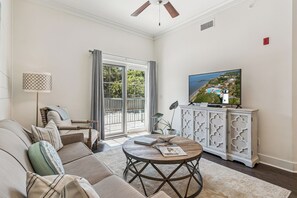 Ein Wohnzimmer mit Sofa, Couchtisch, Fernseher und Blick auf einen Pool und Gebäude.