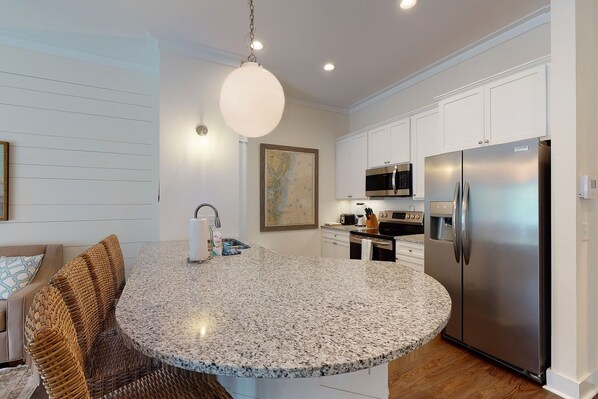 A modern kitchen with white cabinetry, a stainless steel refrigerator, a microwave, and a granite countertop.