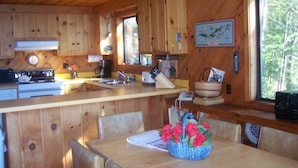 Ein Interieur einer Holzhütte mit Küche, Essbereich und großen Fenstern.