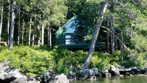 Eine Holzhütte, umgeben von dichtem Wald und einem Gewässer.