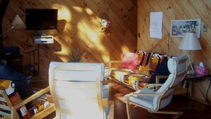 Ein gemütliches Blockhaus-Interieur mit Holzbalkendecke, einem Bett mit farbenfroher Bettwäsche, einem Fernseher und einem kleinen Tisch mit Lampe.