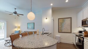 Una cucina con isola centrale, una ventola a soffitto, una lampada a sospensione, una mappa appesa al muro e un'area pranzo con sedie in vimini.