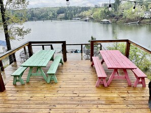 Un muelle de madera con mesas de picnic y vista a un lago con barcos.