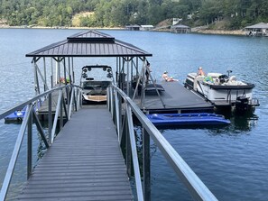 Un muelle de madera que conduce a una zona cubierta para el lanzamiento de embarcaciones, con un bote pequeño amarrado al final.