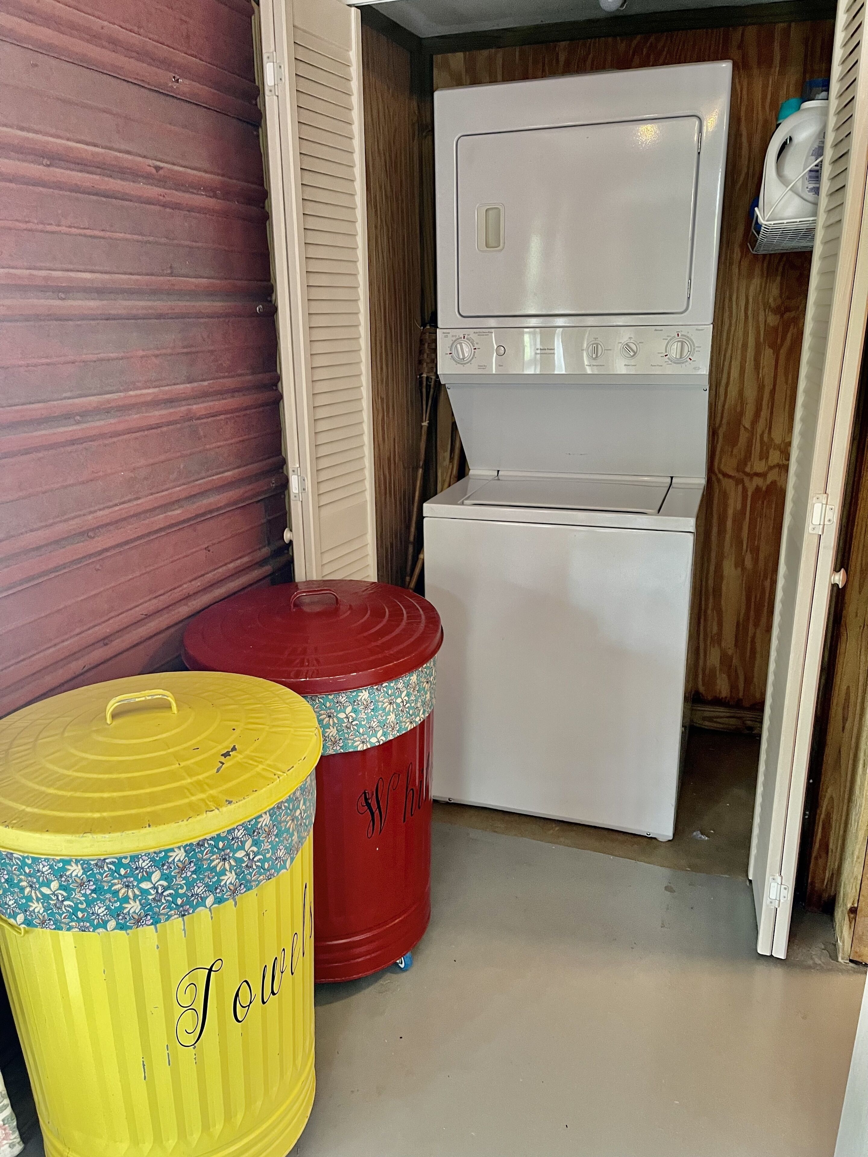 A laundry room with a washing machine and dryer, two trash cans, and a wooden wall.