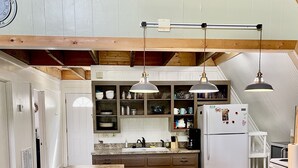 Una cocina con una isla central, taburetes de bar, luces colgantes y un refrigerador.