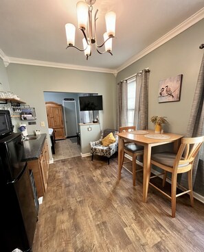 A kitchen with a dining table, chairs, a chandelier, a television, and a wooden cabinet.
