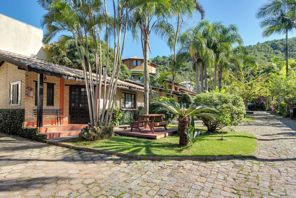 A courtyard with a cobblestone path, a wooden bench, and a picnic table surrounded by palm trees and greenery.