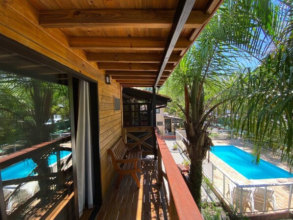 A wooden deck with a pool, a bench, and a view of a pool area.