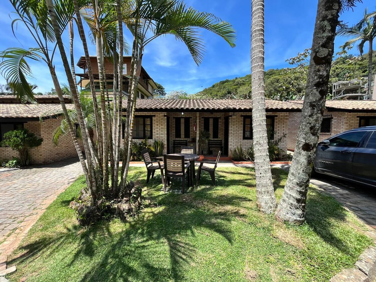 A house with a tiled roof, a patio with a table and chairs, and a car parked nearby.