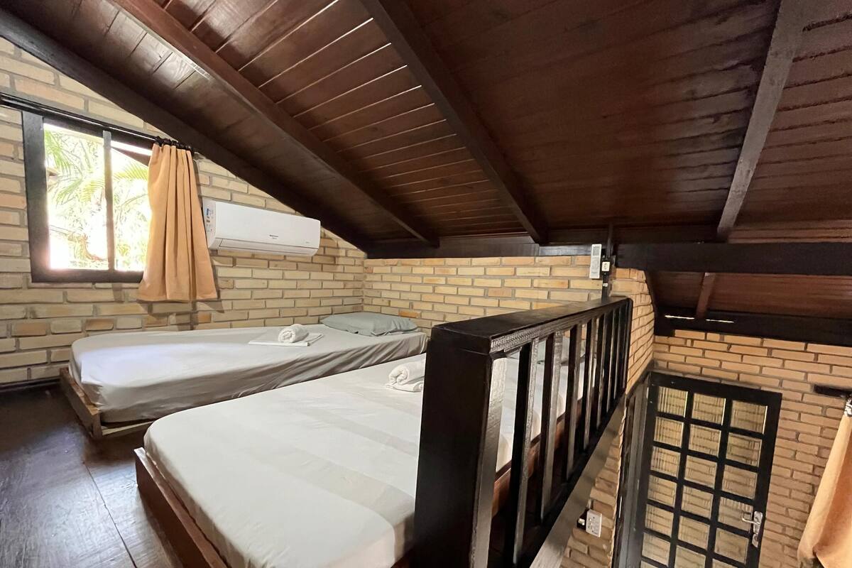 Ein Zimmer mit zwei Betten, Holzbalken, Backsteinwänden und einer Klimaanlage.