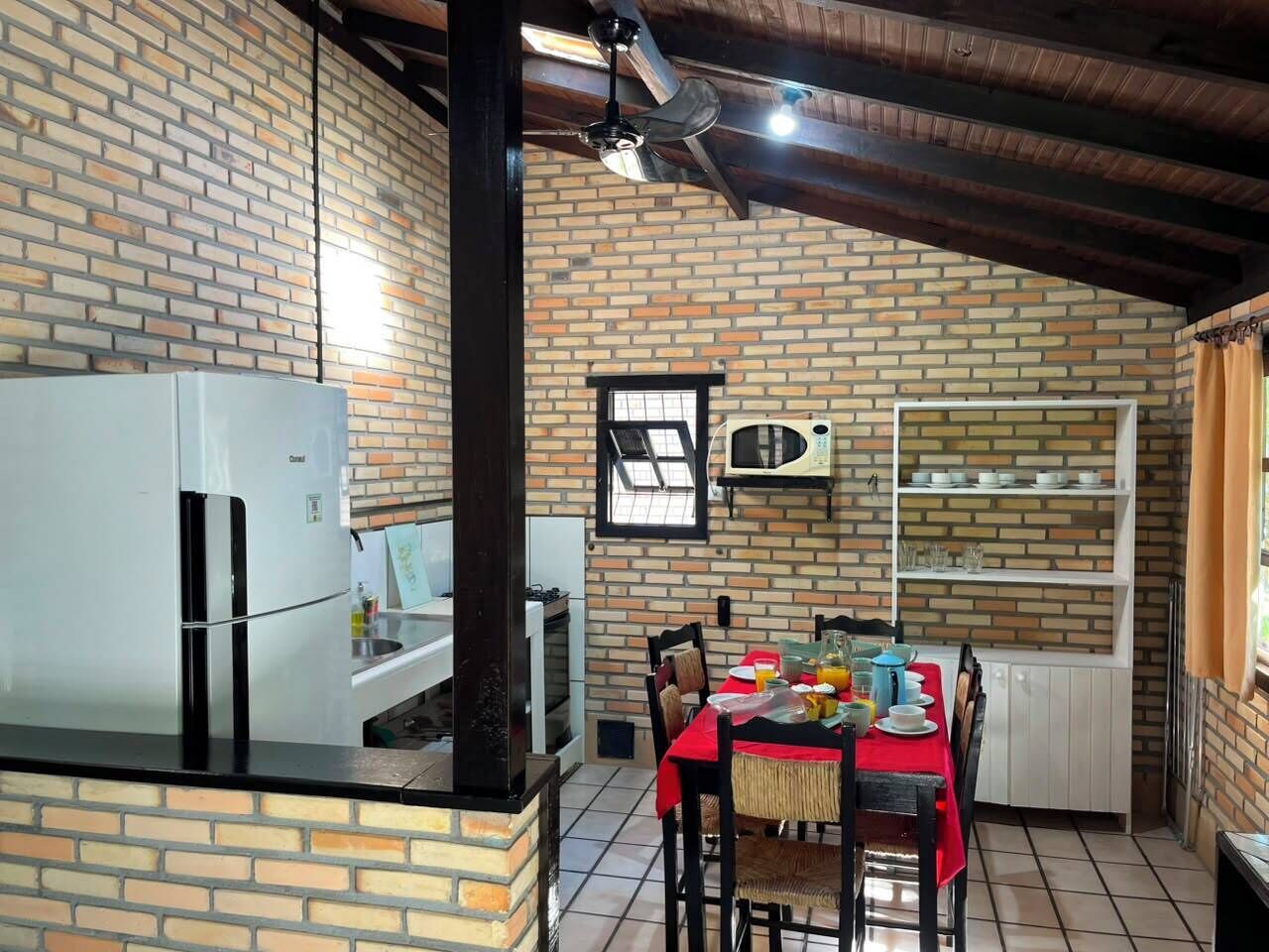 Una cucina con parete in mattoni, frigorifero, forno a microonde e un tavolo da pranzo apparecchiato con piatti e tazze.